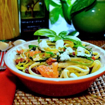 Zucchini spaghetti with linguine in an orange bowl with basil garnish.
