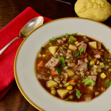 A gold rimmed bowl holds some beef barley soup.