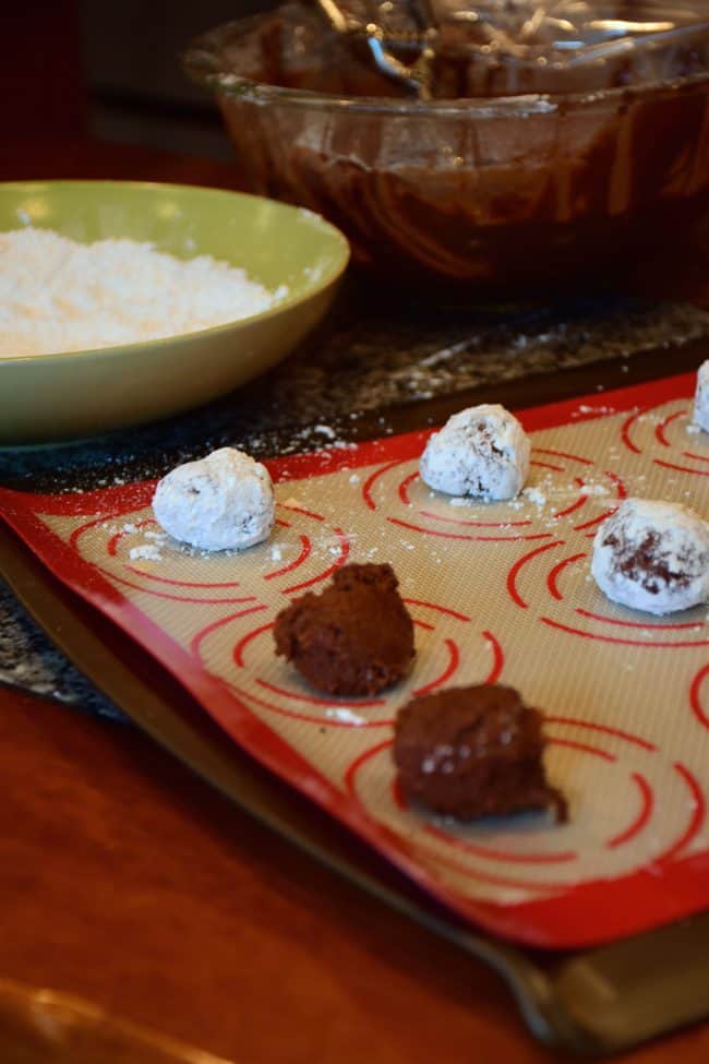 Chocolate Crinkle Cookies being dipped in confectioner's sugar.