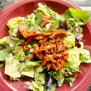 Buffalo chicken on butter leaf lettuce in a red bowl.