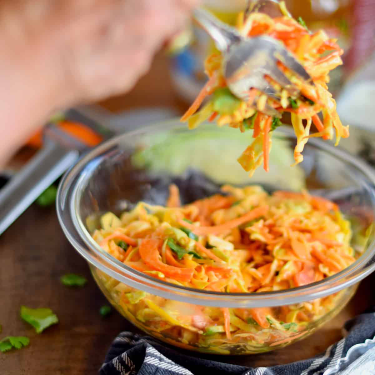 Serving some Coleslaw with Easy Homemade Sriracha Dressing from a glass bowl with a fork and spoon.