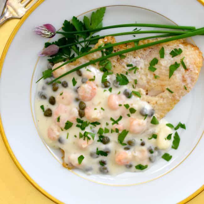 A plate with sole, shrimp, cream sauce, and capers.