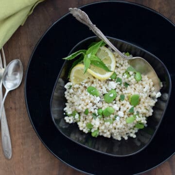 Israeli Couscous with Favas, Feta and Mint in a black bowl with a spoon.