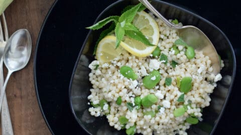 Israeli Couscous with Favas, Feta and Mint in a black bowl with a spoon.