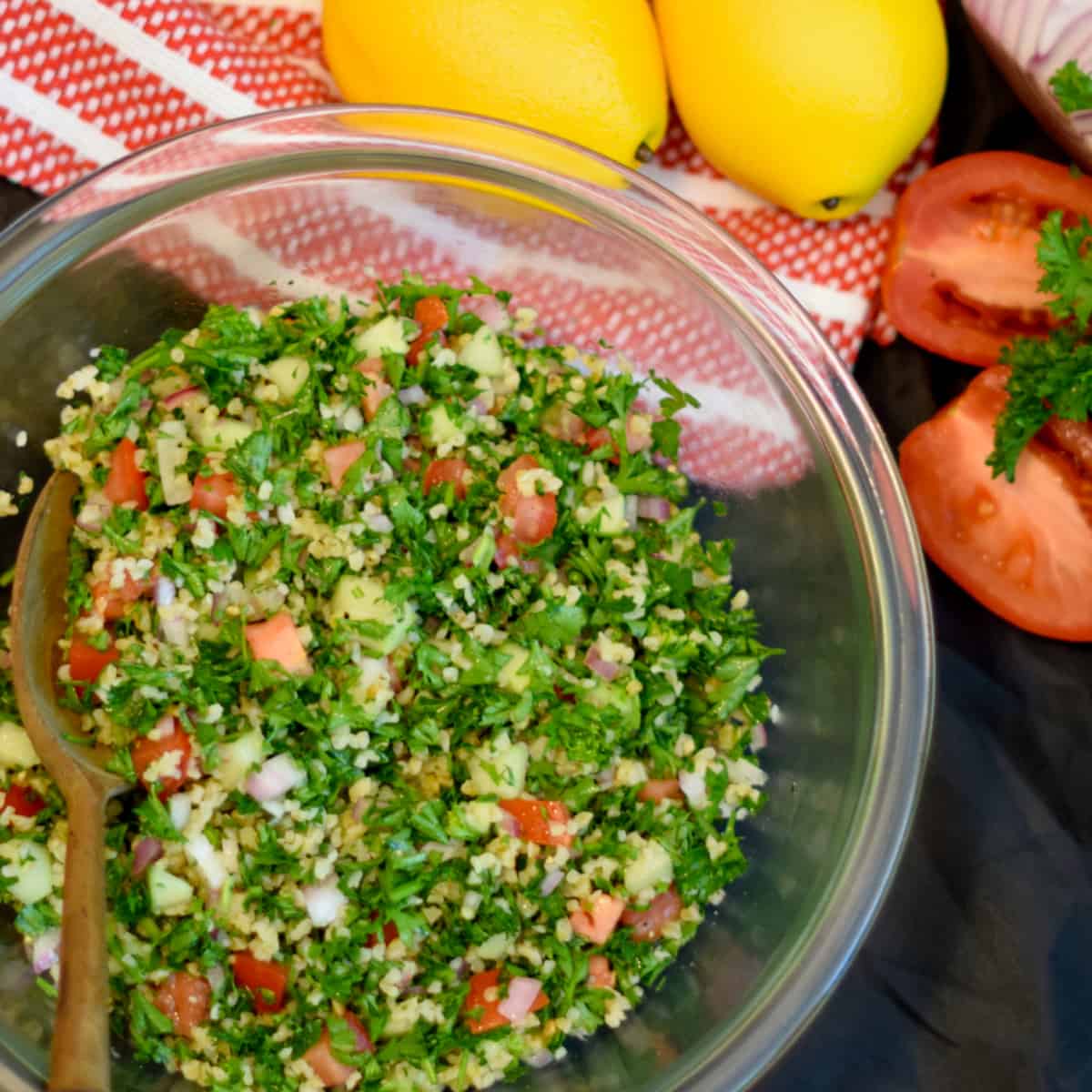 Lemons, tomato halves, and a red towel enhance this picture of Tabouleh Salad.