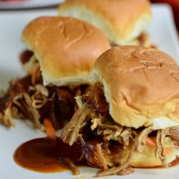 Three. pulled pork sliders with bbq sauce and coleslaw on a white plate.