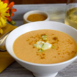 Curry soup in a white bowl with flowers behind.