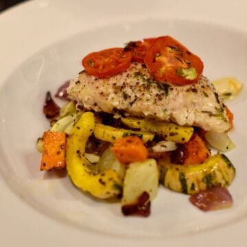 A white bowl with oven poached chicken along with roasted squash and tomatoes.