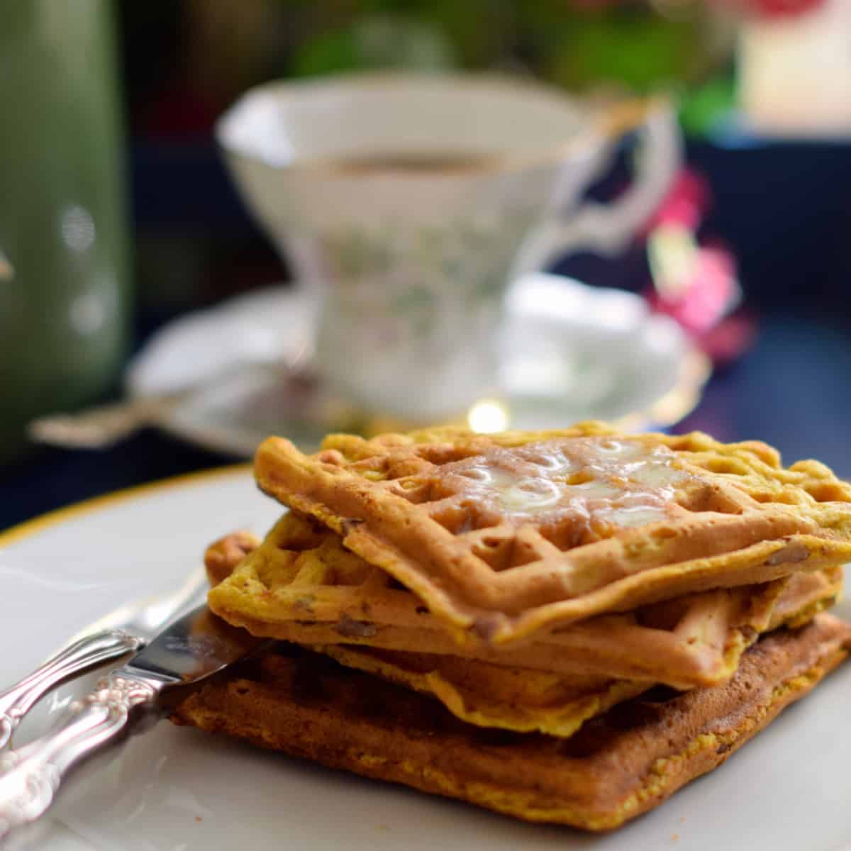 A stack of Pumpkin Buttermilk Pecan Waffles with an antique coffee cup.
