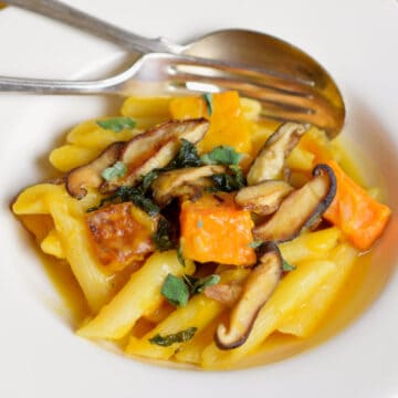 A white bowl with pasta, butternut squash, and shiitake mushrooms.