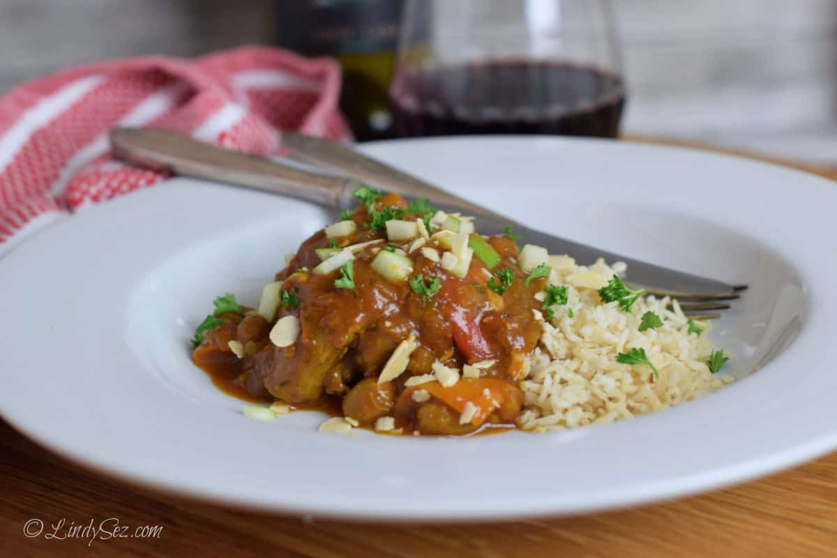 Cooked Indian spiced chicken on a plate with rice and a glass of wine.