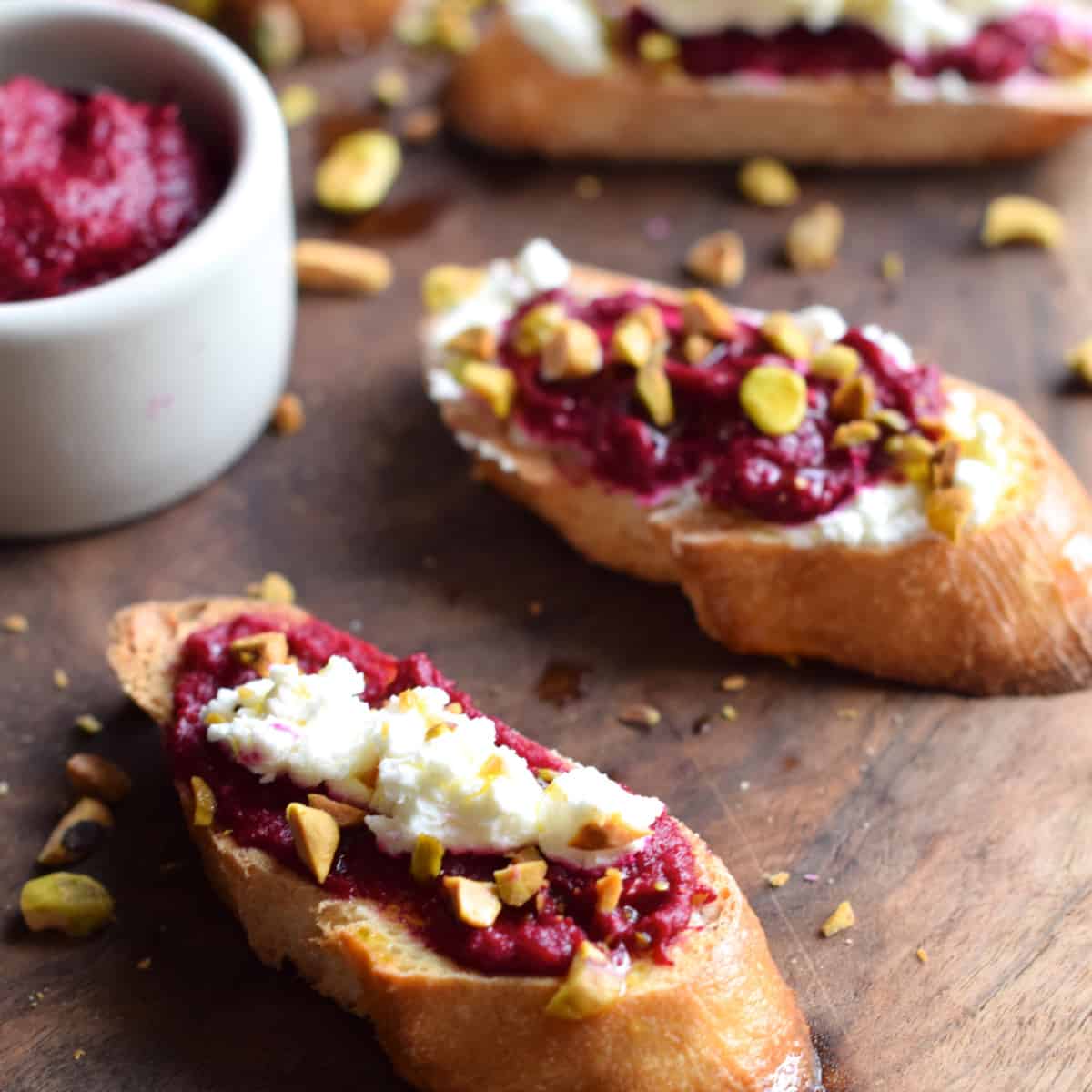 Roasted Beet Crostini with Goat Cheese and Pistachio on a wooden board.