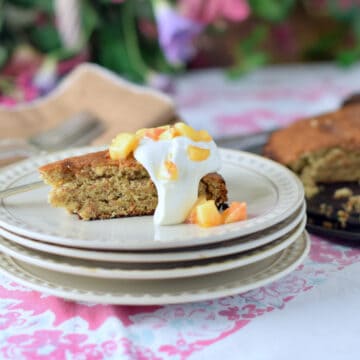 Fresh Peach Almond Torte with whipped cream and fresh peaches on a stack of white plates.