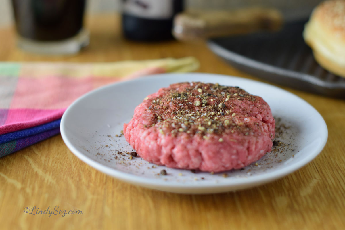 A hamburger on a plate with coffee rub and black pepper.