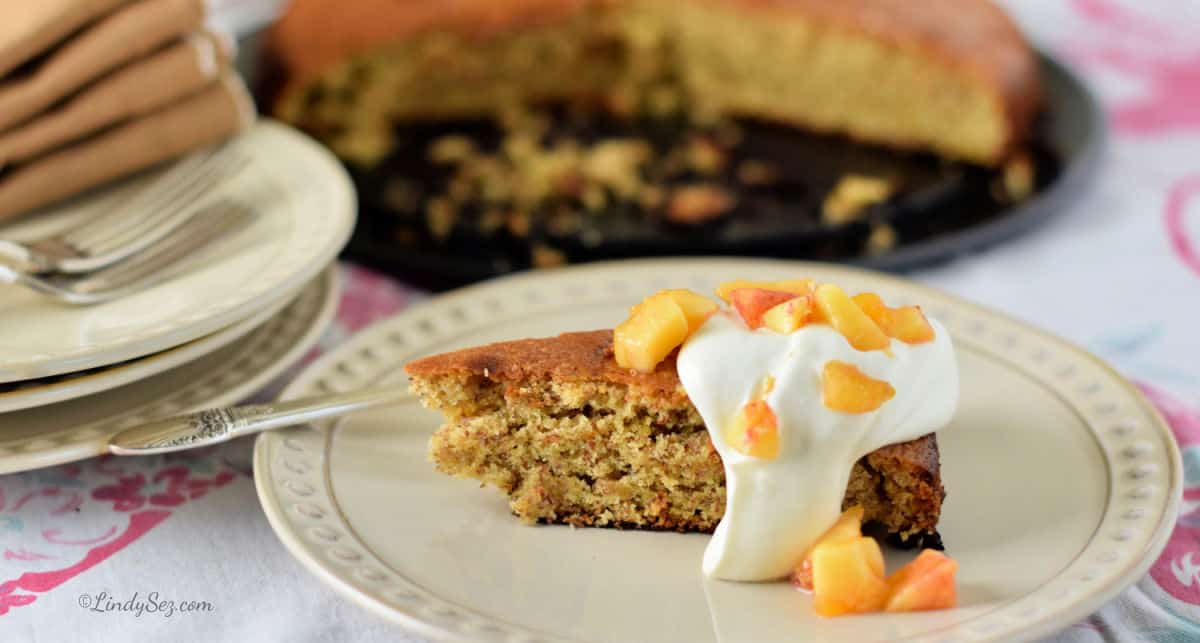A close-up of a slice of peach almond torte with fresh whipped cream and fresh peaches.
