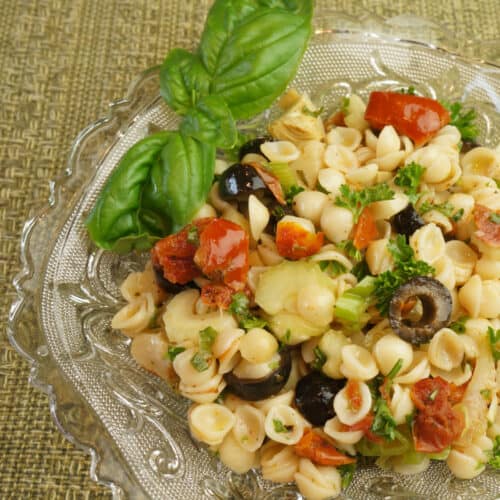 An antique glass bowl holds colorful pasta salad with sun dried tomatoes.