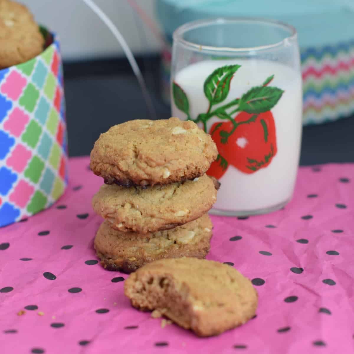 A stack of thick almond butter cookies on.a bright pink mat with a glass of milk.