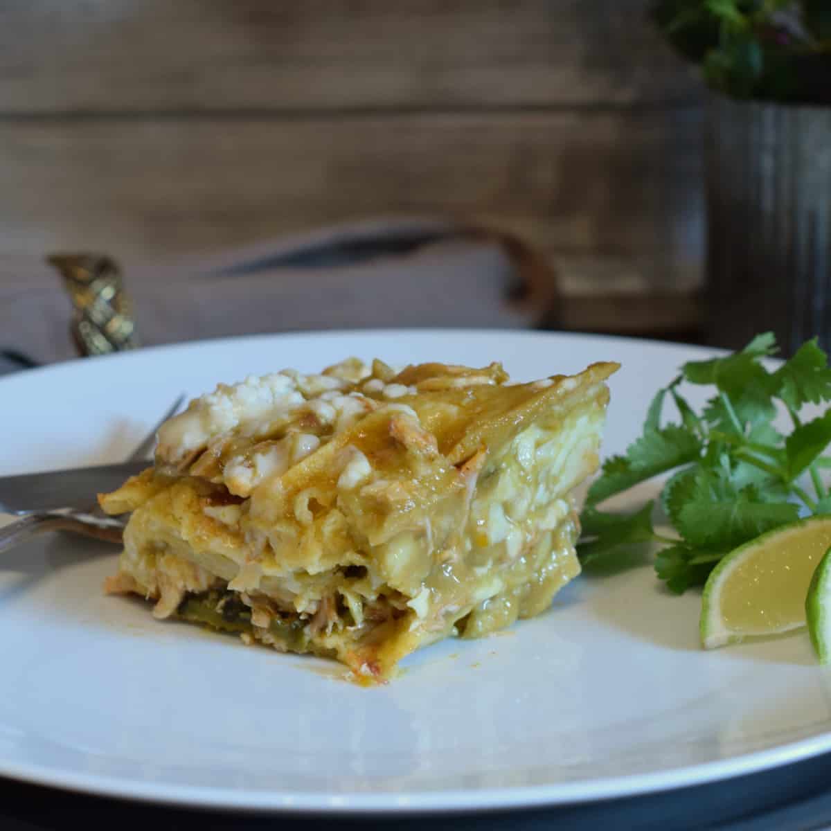 Green Chile Chicken Enchilada Stack on a plate with cilantro and lime garnishes.