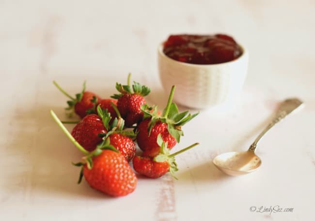 Fresh strawberries along side a dish of fresh Easy Strawberry Jam with Balsamic and a silver spoon.