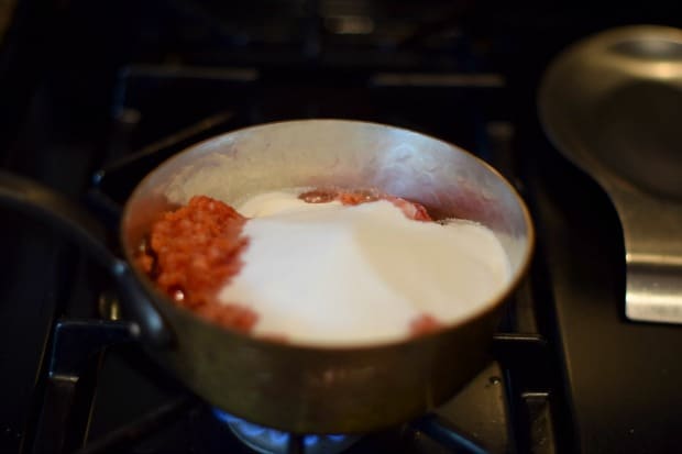 adding sugar to the pot of easy fresh strawberry jam with balsamic on the stove.