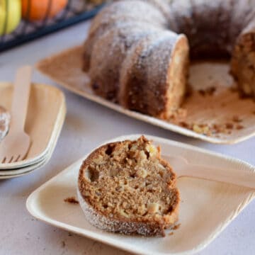 A slice of Fresh Apple Chunk Olive Oil Cake has been removed from the cake and sits on a bamboo plate.