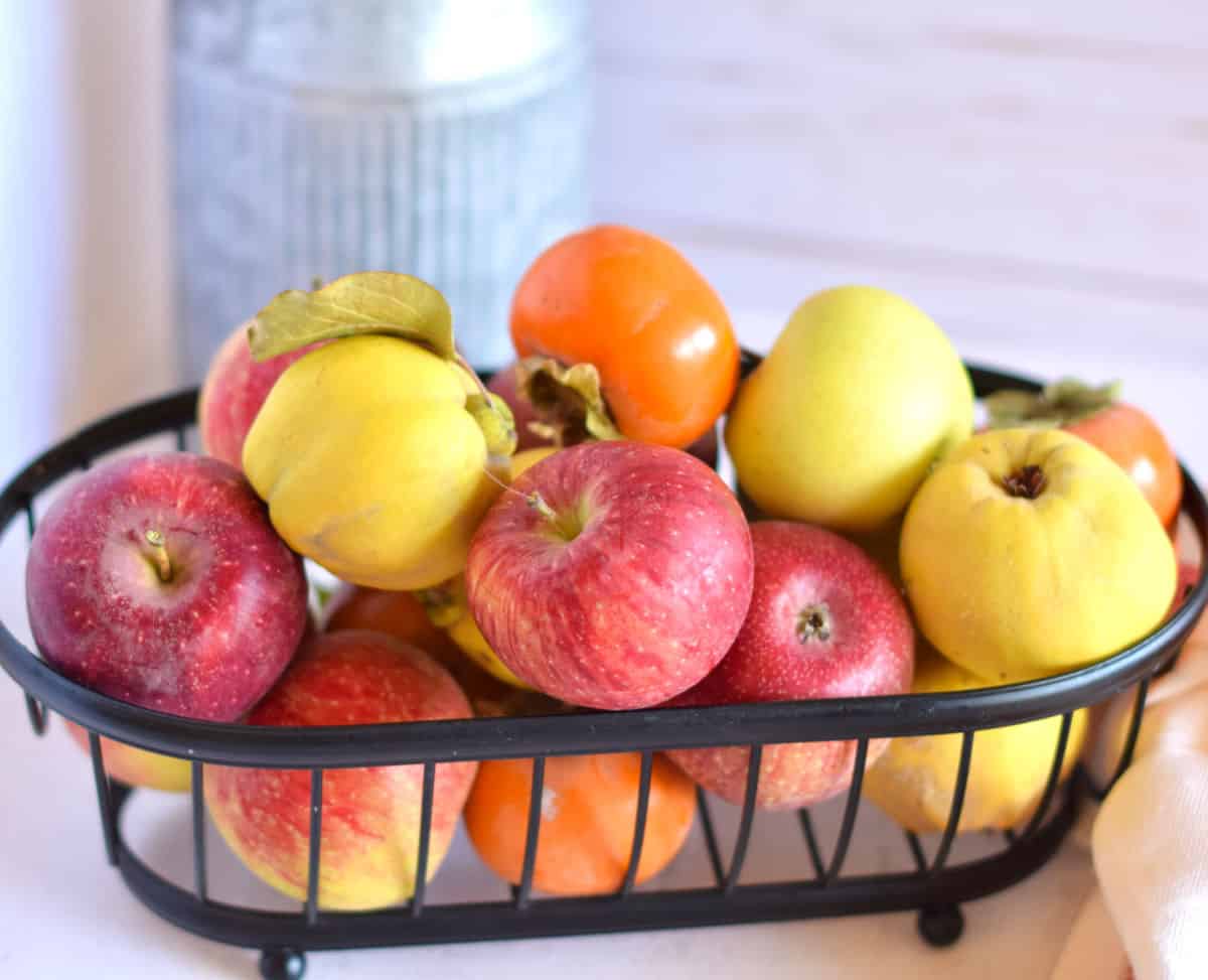 A basket with a variety of apples and othr fall fruit.