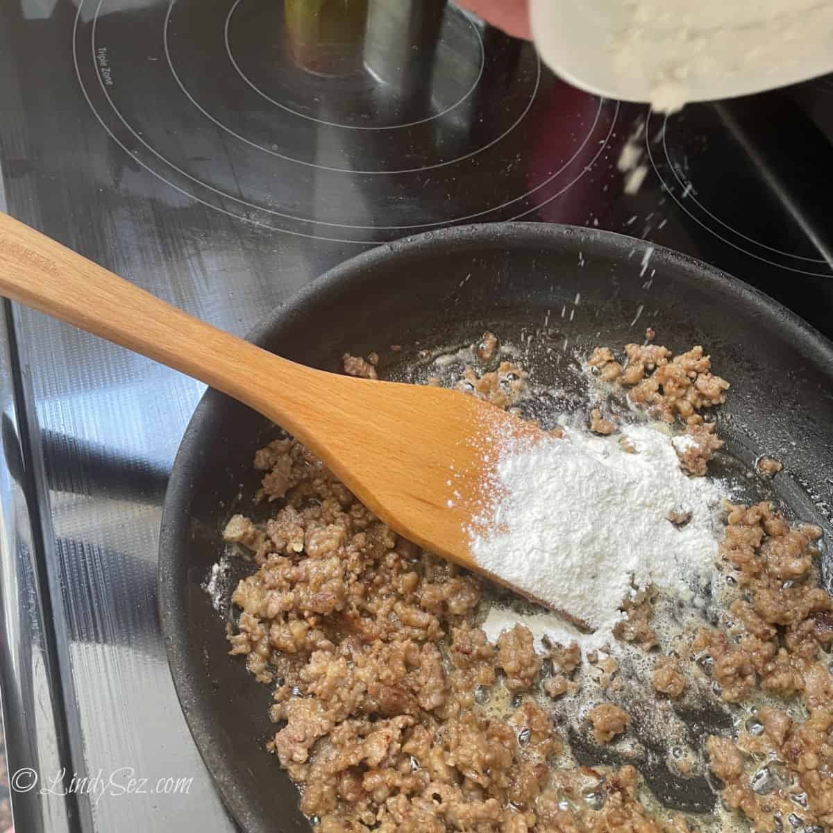 Adding flour to sausage meat in a skillet.