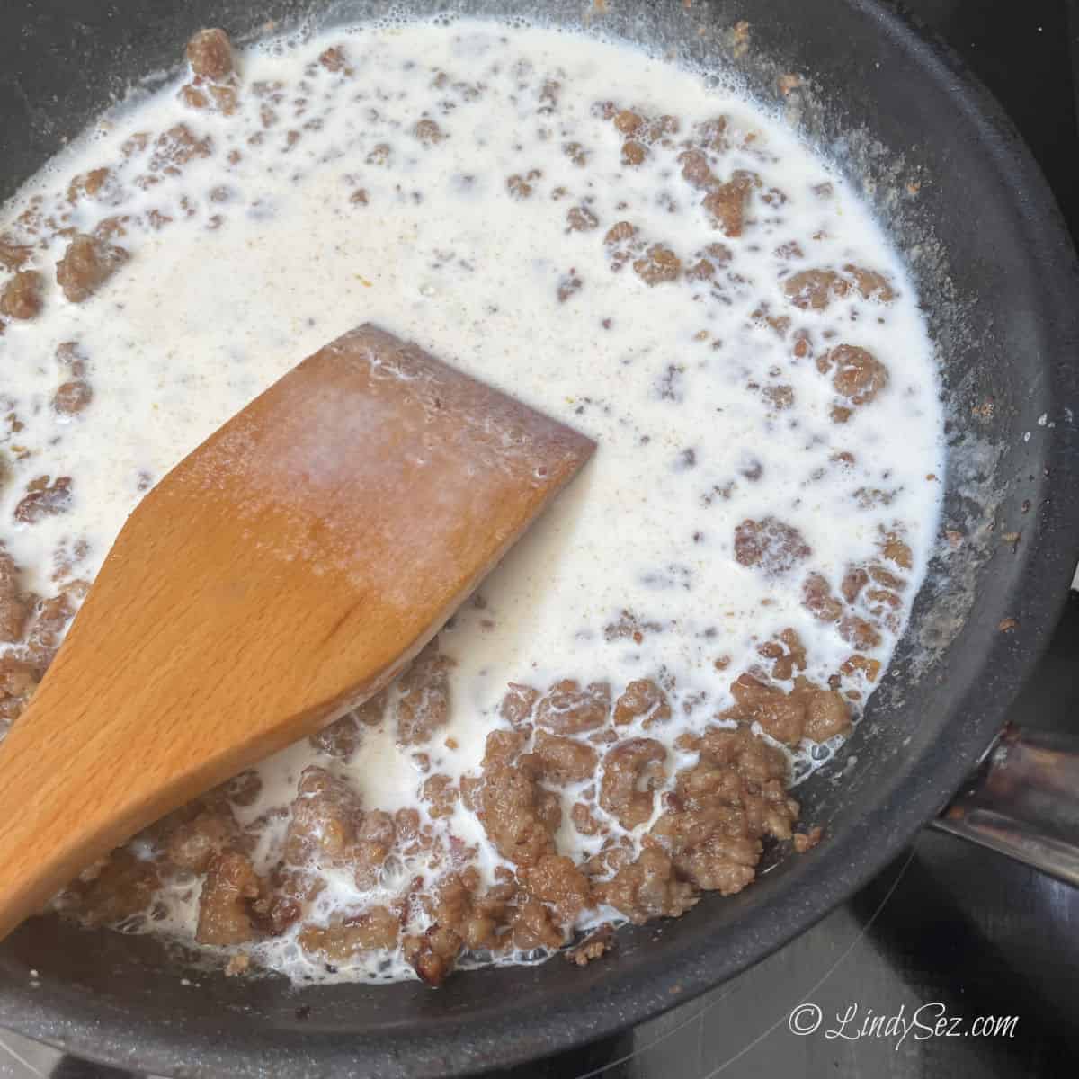 Adding milk to sausage to make gravy.