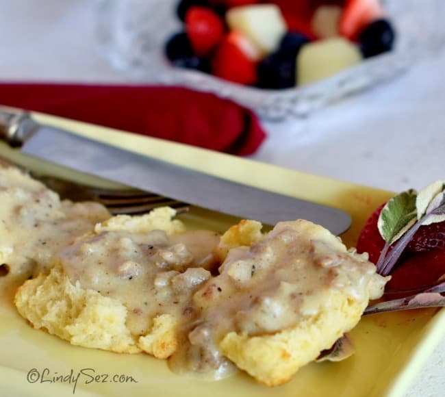 Simple sausage gravy on a yellow platter with fruit salad in the background.