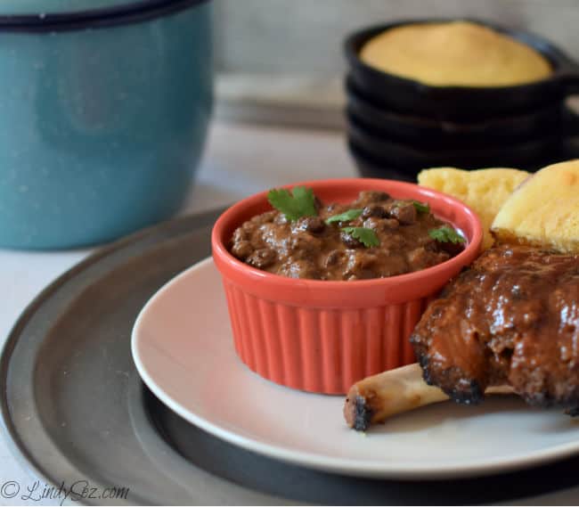 A serving of Spicy Black Beans in an orange bowl with some tasty ribs.