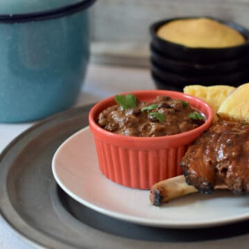 A bowl of spicy black beans being served with juicy ribs and cornbread.
