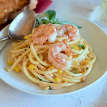 Pink shrimp sit on top of bucatini pasta with corn and pine nuts.