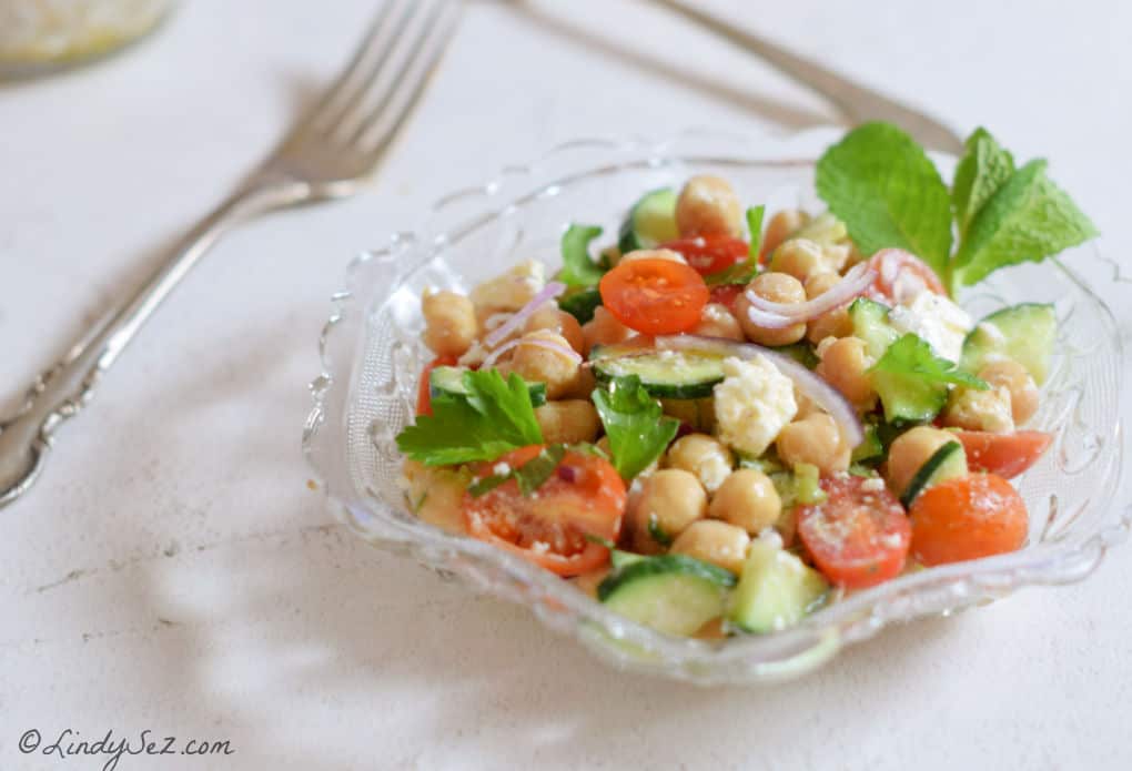 A.glass bowl with Chickpea Salad filled with bright veggies.