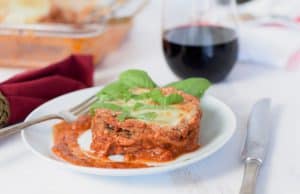 A dish of Easy Low-Fat baked eggplant parmesan with a glass of wine and the baking dish.