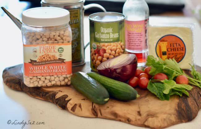 The ingredients for Mediterranean Chickpea salad sitting on a piece of wood.
