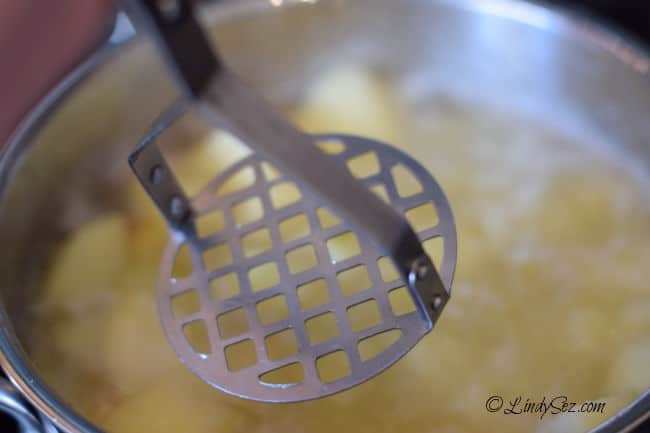 Using a potato masher to mash the cooked apples in this easy sweet tart homemade applesauce.