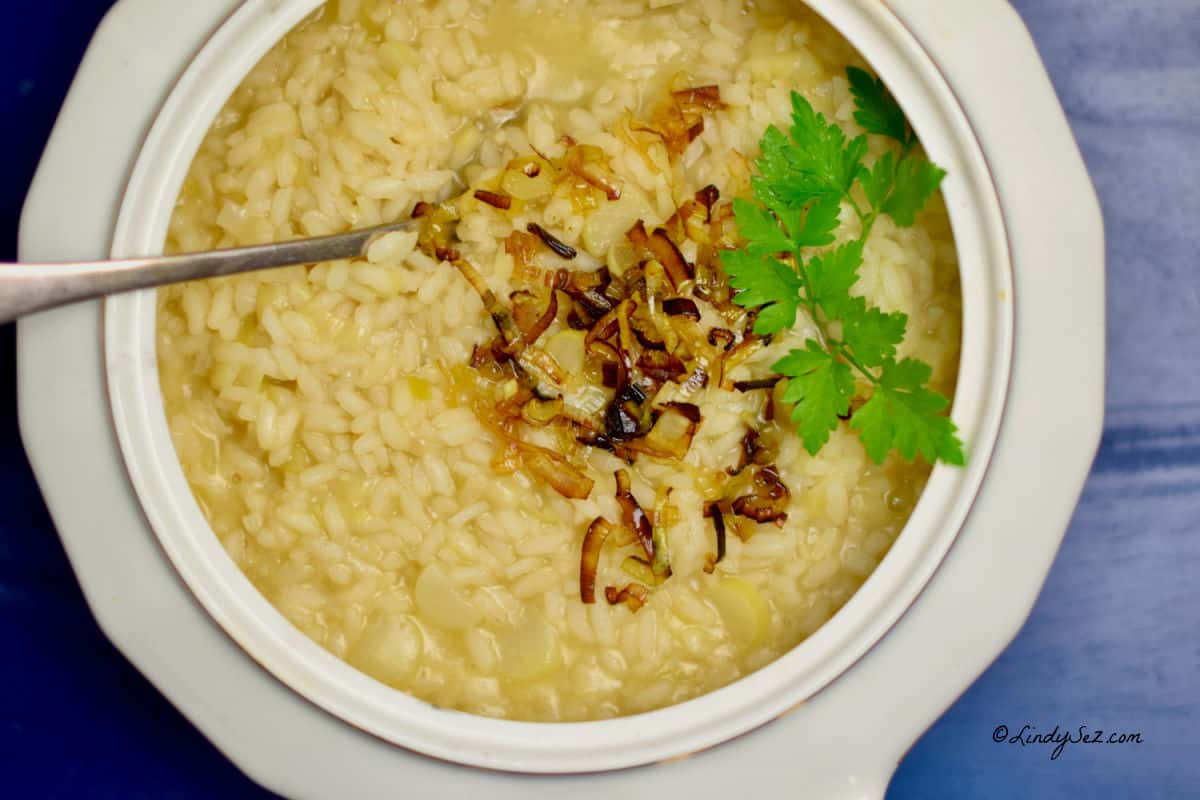 A white bowl with spring risotto, caramelized leeks and a parsley garnish.