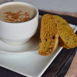A square white plate holds a cup of coffee and some pumpkin biscotti.