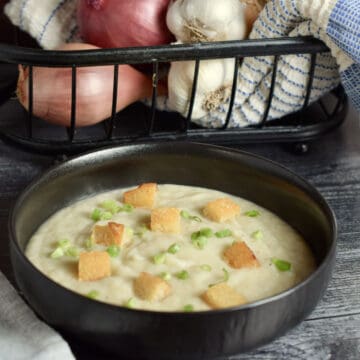 5-Onion soup in a black bowl with a variety of onions in the background.