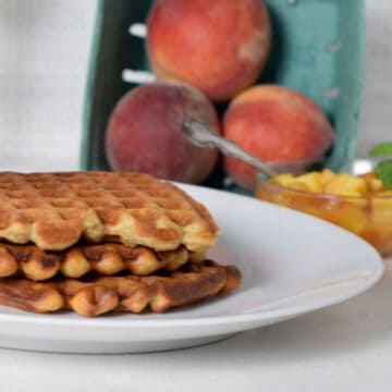 a stack of waffles with fresh whole peaches in a green box.