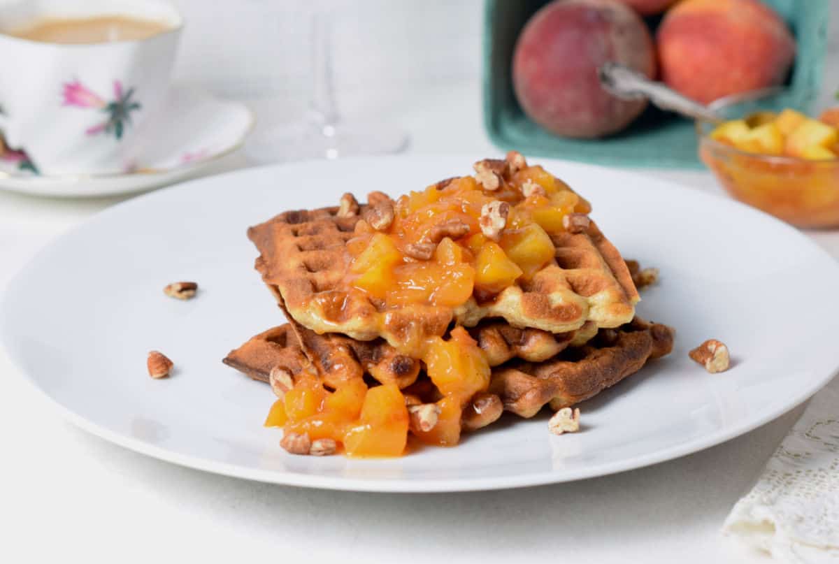 A white plate with a waffle topped with peach compote.