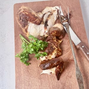 Cut up chicken on a wood cutting board with a knife and antique fork.